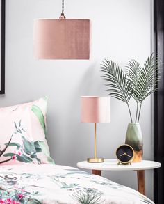 a bed with pink and green pillows, two lamps and a plant on the end table