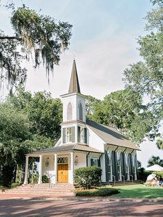 a white church with a tall steeple surrounded by trees