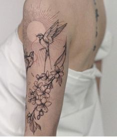 a woman's arm with a bird and flowers tattoo on the left side of her arm