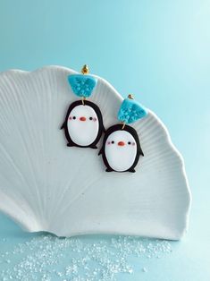 a pair of penguin earrings sitting on top of a shell