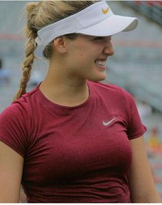 a woman in a red shirt and white visor holding a tennis racket