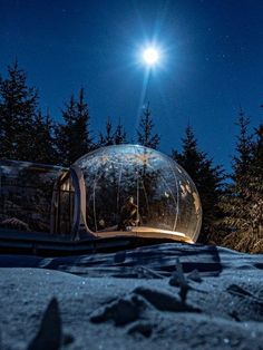 a person standing in front of a glass dome on top of snow covered ground at night