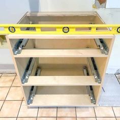 an unfinished kitchen cabinet with yellow handles and drawers on the bottom shelf, in front of a tiled floor