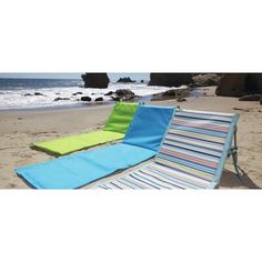 two lounge chairs sitting on top of a sandy beach next to the ocean with rocks in the background