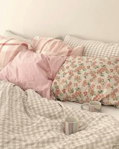 a bed with pink and white pillows on top of it next to two mugs