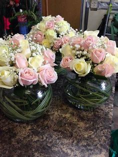 three clear vases filled with pink and white flowers on a counter top next to other glass vases