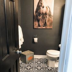 a bathroom with black and white tile flooring and a painting on the wall above the toilet