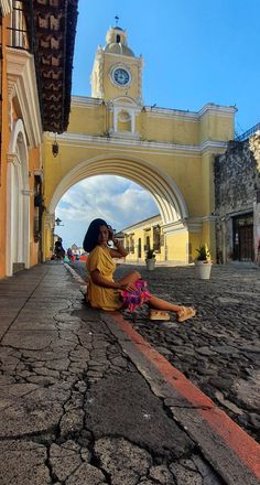 a woman sitting on the ground talking on her cell phone in front of an archway