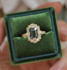 a person holding an engagement ring in a green velvet box with diamond trimming around the band