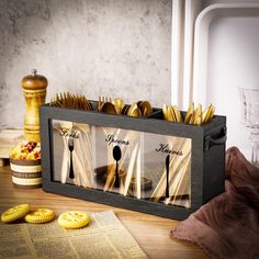 a wooden box filled with forks and spoons on top of a table next to cookies