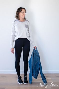 a woman standing in front of a white wall with a jacket on her lap and jeans hanging up against the wall