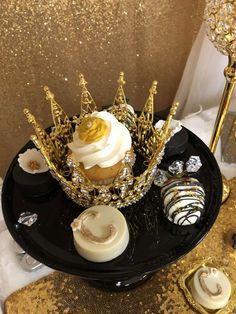 a black plate topped with cupcakes covered in white frosting and gold crown decorations