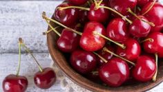 a red bowl filled with cherries on top of a wooden table