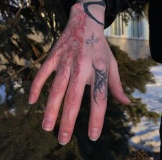 a person's hand with tattoos on it in front of some snow covered trees