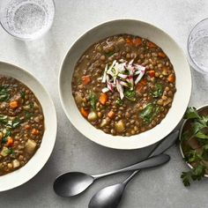 two bowls filled with lentula soup next to silver spoons on a white table