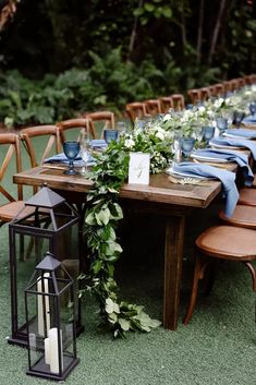 an outdoor table set up with blue linens and greenery