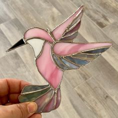 a hand holding a pink and white stained glass hummingbird