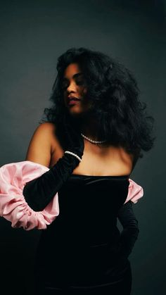 a woman in a black dress with a pink ruffle on her sleeve and pearl necklace