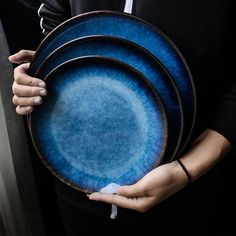 a person holding three blue plates in their hands and one is wearing a black shirt