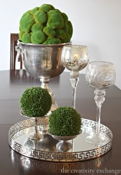 there is a silver bowl with green balls in it and two wine glasses on the table