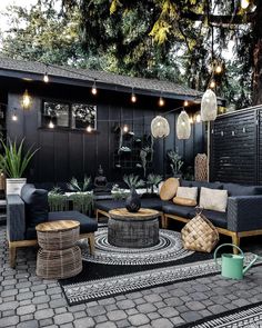 an outdoor living area with black furniture and lights hanging from the ceiling, surrounded by potted plants