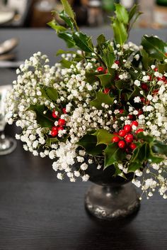 a vase filled with white flowers and red berries