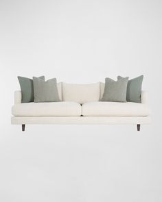 a white couch with four pillows on it's back and one pillow hanging off the side