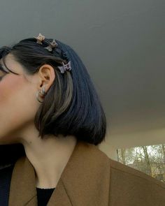 a close up of a person with short hair wearing ear clips and a brown coat