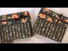 two black boxes with flowers on them are sitting side by side, one is open and the other has a bow at the top