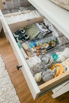 an open drawer filled with baby items on top of a wooden floor next to a bed