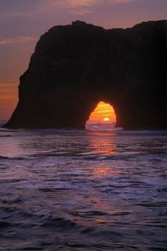 the sun is setting behind an arch in the ocean