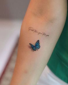 a small blue butterfly tattoo on the left arm with words above it that says, you are