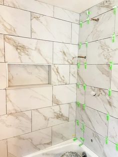 a bathroom with white tile and green tape on the shower wall next to a bathtub