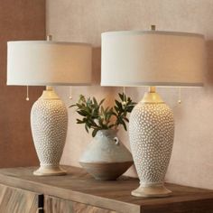 two white vases sitting on top of a wooden table next to lamps and a plant