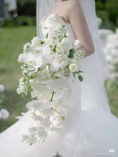 a woman in a wedding dress holding a bouquet of white orchids and greenery