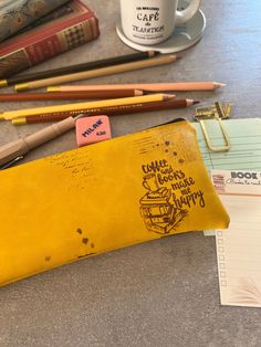 a yellow pencil case sitting on top of a table next to some pens and paper