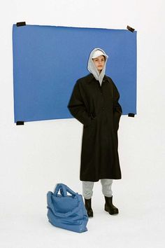 a woman standing in front of a blue sign with a bag on the ground next to it