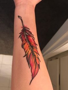 a woman's arm with a red and orange feather tattoo on the left wrist