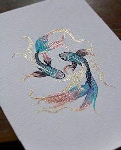 two gold and blue koi fish are depicted on a white card that is laying on a wooden table