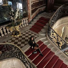 a woman is sitting on the stairs in an ornate building with red carpet and gold railings