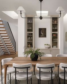 a dining room table with white chairs and a potted plant on top of it