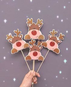 a hand holding four reindeer cupcake toppers on a stick with stars in the background