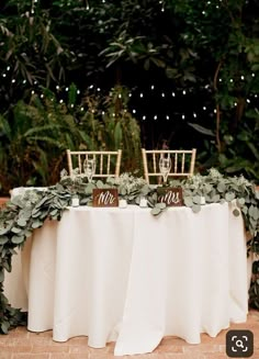 the table is set up with chairs and greenery