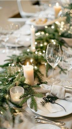 the table is set with white plates, silverware and greenery for christmas dinner