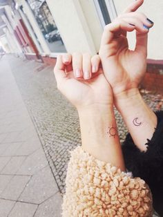 two people with matching tattoos on their wrists holding hands up to each other and pointing fingers at the camera