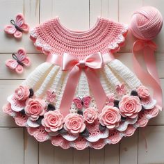 a crocheted dress with pink flowers and butterflies on the side, next to a ball of yarn