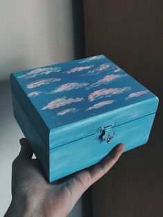 a hand holding a blue box with clouds painted on it