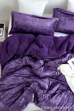 a purple comforter and pillows on a bed in a room with white walls,