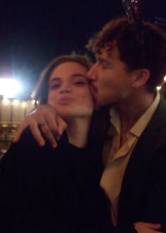 a man and woman kissing each other in front of an arena at night with bright lights