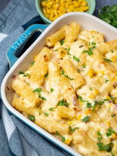 a white casserole dish filled with pasta and corn on the table next to it